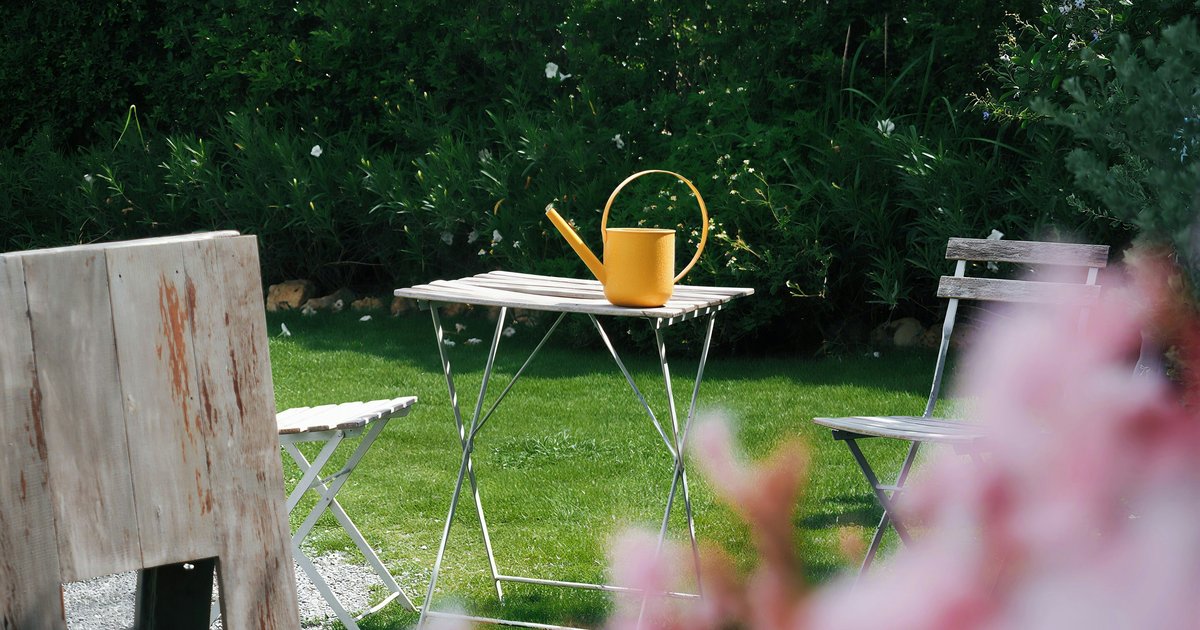 A sunny garden with chairs, a table and a yellow watering can